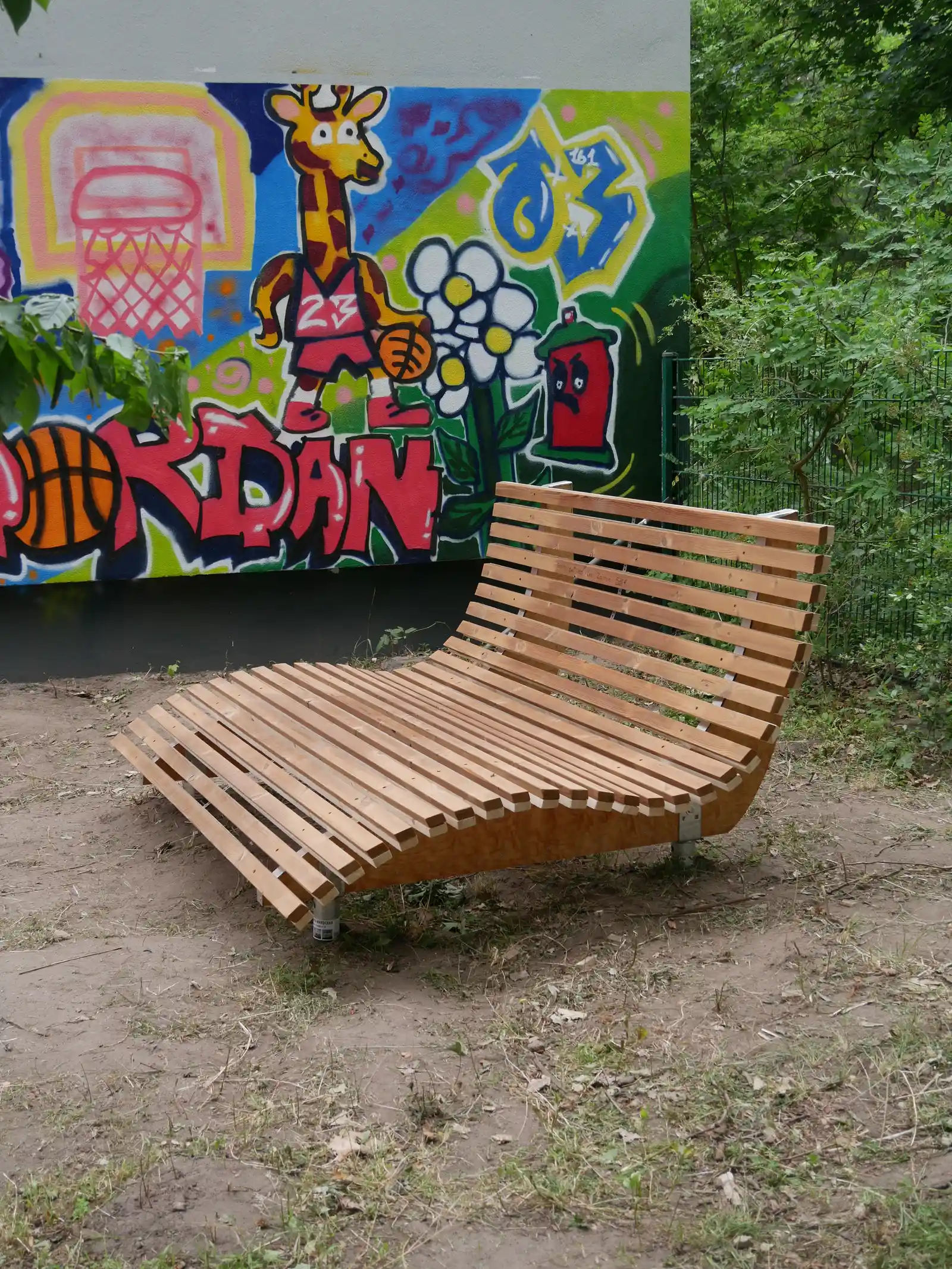 Eine selbst gebaute Holzliege steht vor einer bunten Graffitiwand.